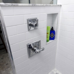 Stainless steel fixtures in white tile open shower